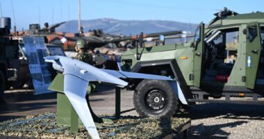 A small fixed-wing drone displayed beside Greek military vehicles during a defense exercise.