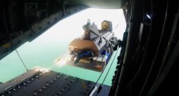 A Kraken K3 Scout uncrewed surface vessel (USV) attached to a Capewell UMCADS delivery platform being jettisoned from the open rear cargo ramp of an Airbus A400M military transport aircraft over the ocean.